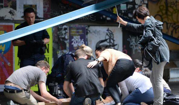 EMERGENCY: Sarah Maclure, pictured in an orange top, helps victims at the intersection of Queen and Bourke streets during Friday's attack. Picture: JUSTIN MCMANUS 