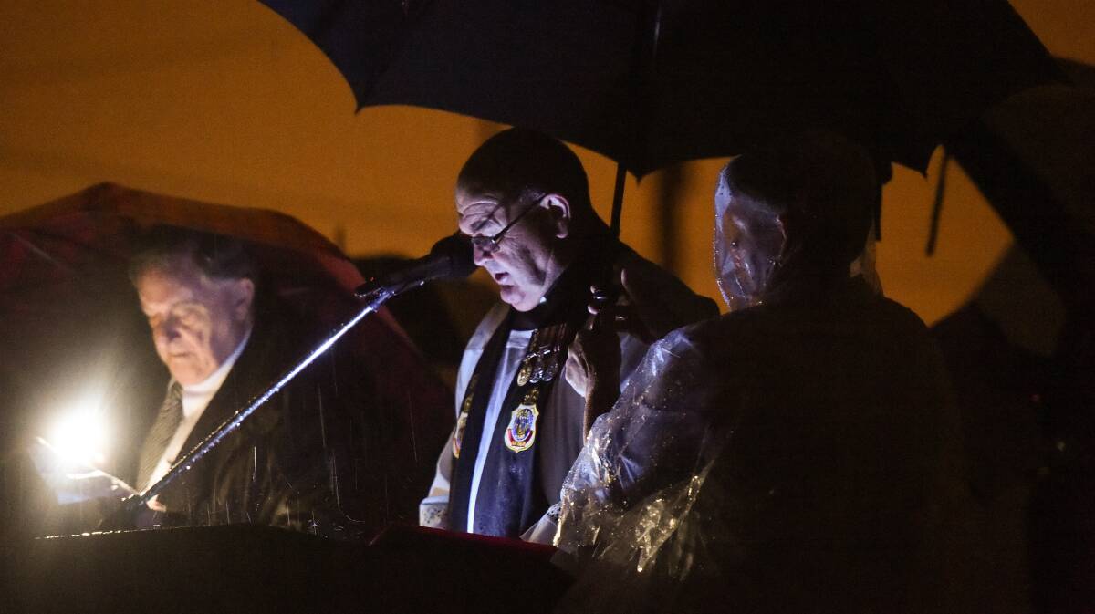 The brolly brigade: Chaplain Father Alan Kelb addresses the Albury dawn service as a helper protects him with an umbrella and master of ceremonies Paul McSwiney checks his notes. Picture: MARK JESSER