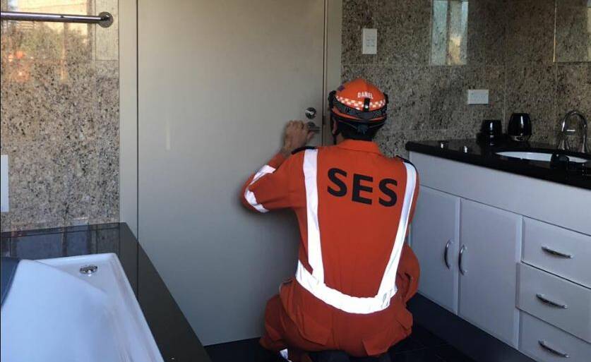 An SES volunteer gets to work on the bathroom door responsible for a man's unfortunate predicament at Kiama, early Monday. Picture: NSW SES Kiama Unit