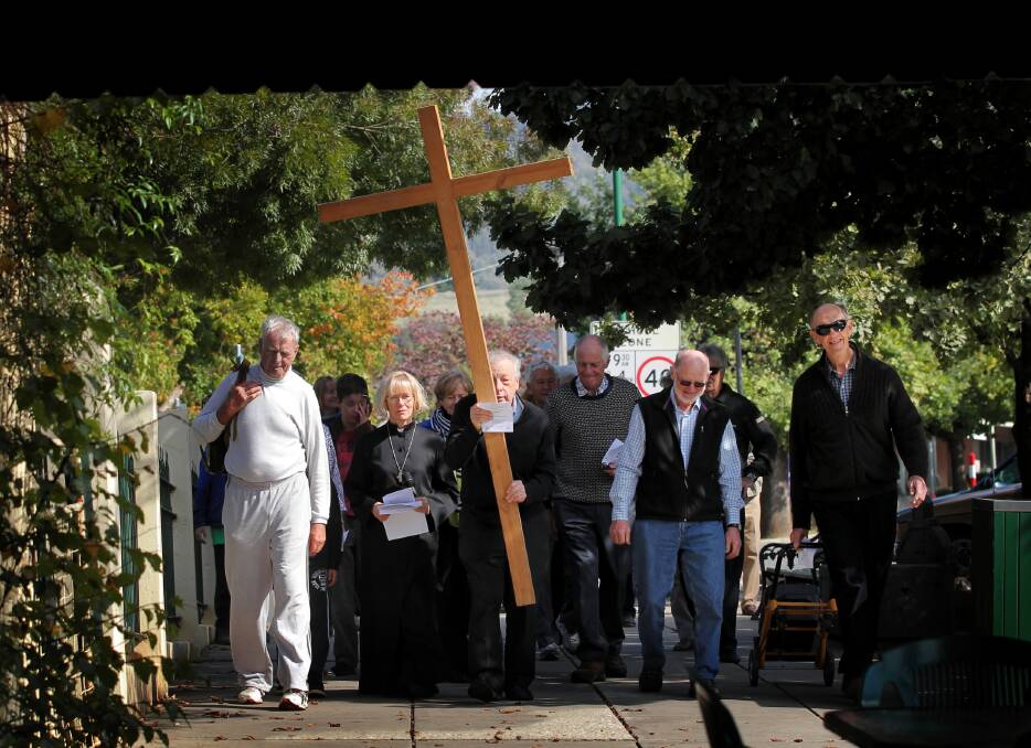 Yackandandah postmaster Warren Gould holds the cross as others, including Reverend Fay Fraser, walk alongside him in High Street. Picture: DAVID THORPE