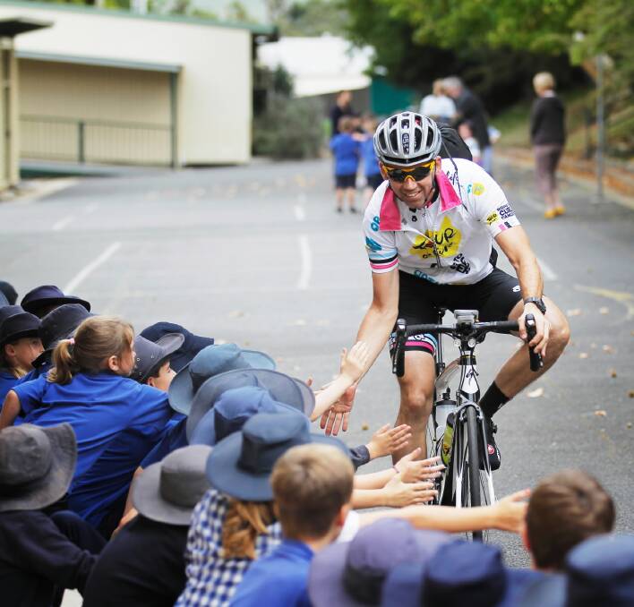 Tour De Cure cyclist Pete Oost, from Brisbane, greets students at Tallangatta Primary School yesterday. INSET: Cyclist Paul Egan and Sunrise weather presenter James Tobin educate Tallangatta students about how to prevent cancer. Pictures: DYLAN ROBINSON