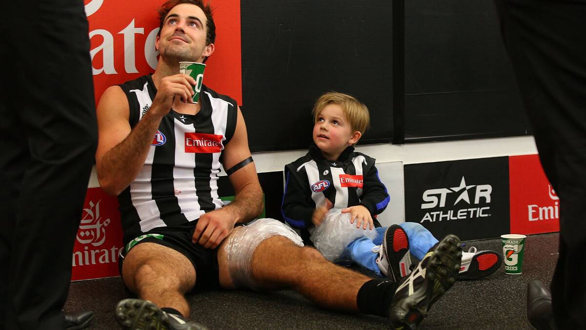 Steele Sidebottom of the Magpies rests after taping a bag if ice to the leg of Ayce Buckley (R) , son of coach Nathan Buckley. Photo: Getty Images. 