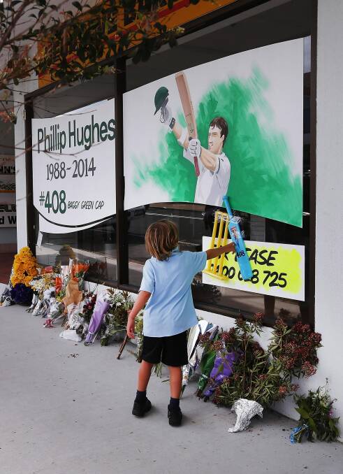 A youngster pays tribute to Phillip Hughes at a shop front in Macksville yesterday. Picture: FAIRFAX