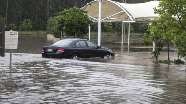 A car navigates flooding in a Burpengary shopping centre carpark in Brisbane on Friday. Photo: Getty Images