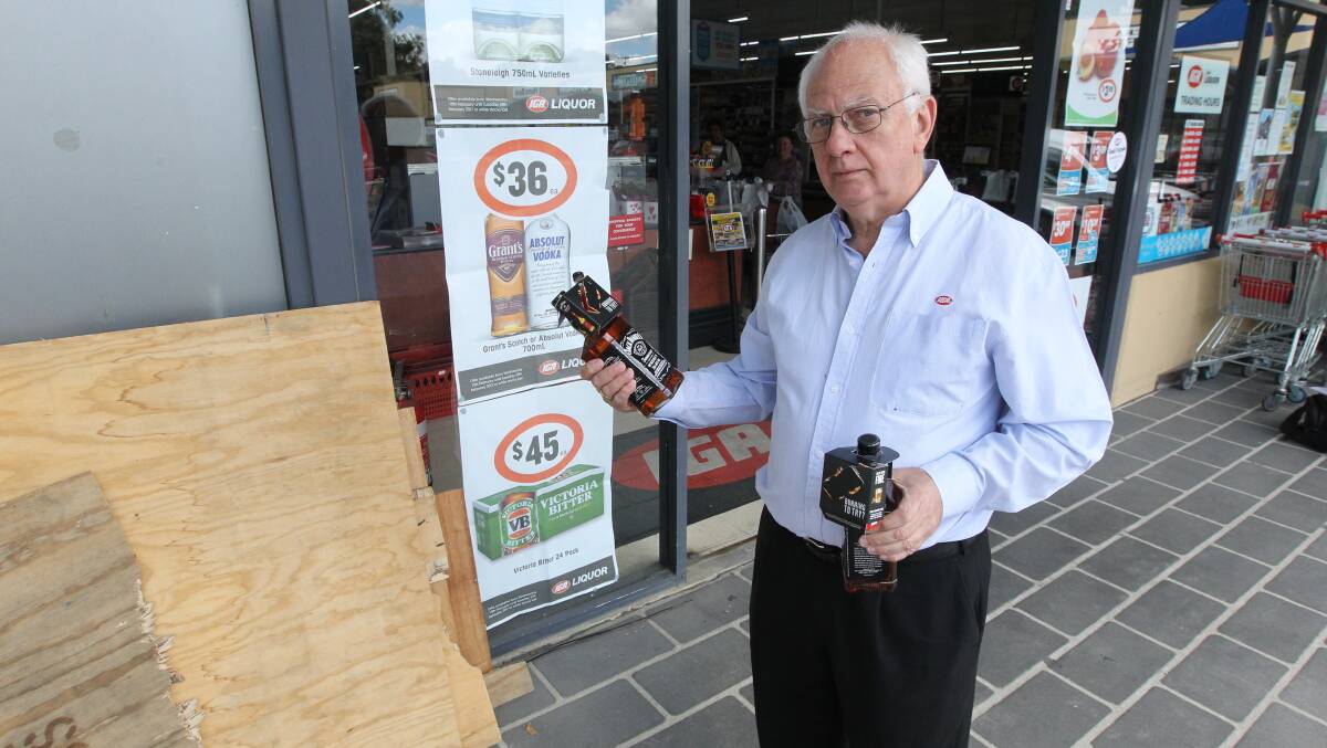DAMAGE: Bob Mathews stands near the smashed doors of the Jindera IGA with bottles targeted during the ram raid. Picture: BLAIR THOMSON