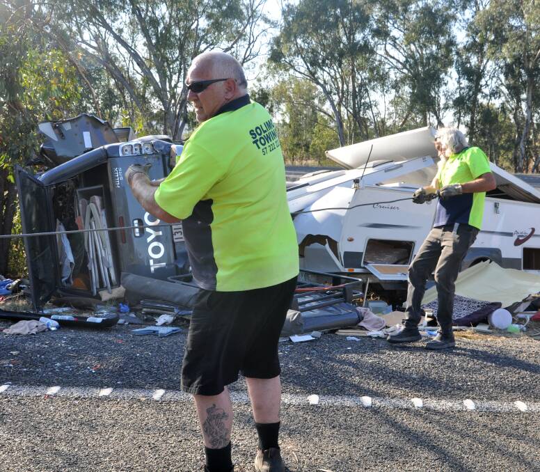 FATAL CRASH: Tow truck workers prepare to remove the couple's car and caravan from the side of the highway. Police are investigating how the vehicle left the road before hitting a tree. Picture: BLAIR THOMSON