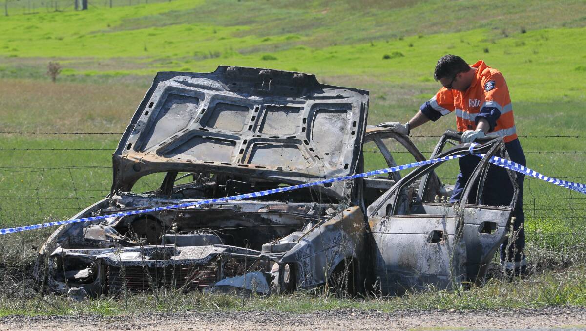 DESTROYED: Detective Graeme Simpfendorfer examines the burnt out car. Pictures: BLAIR THOMSON