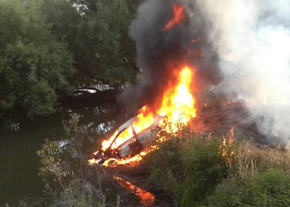 Flames erupt from a car after it was dumped on banks of a tributary of the river. Picture: DAVID HAWKINS