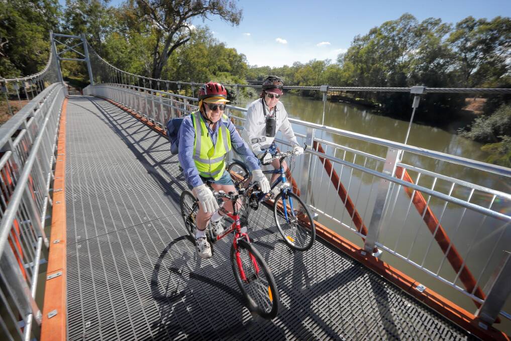 Jim Costelloe and Russell Cochran, both of Wodonga, ride over the new suspension bridge on Saturday. Mr Cochran watched the old bridge being built and is impressed with its replacement. Picture: TARA GOONAN