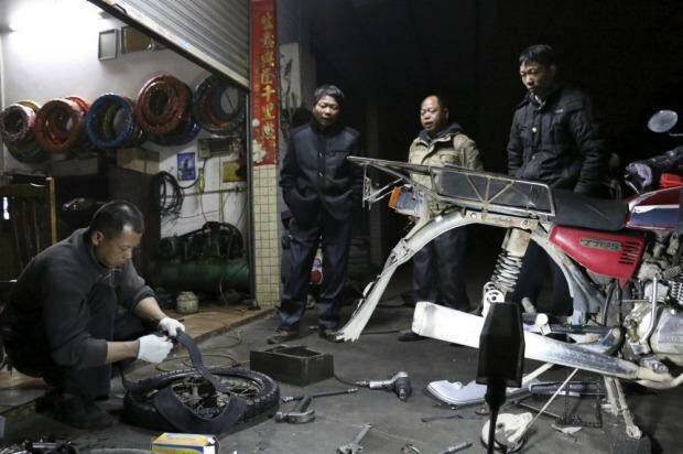  Lu Qiao and his  brothers watch as a roadside mechanic replaces a tyre on their motorcycle.  Photo: Sanghee Liu