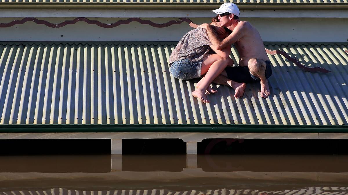 A man comforts his daughter on their roof as they inspect damage to their neighbourhood in Bundaberg. Photo: GETTY IMAGES