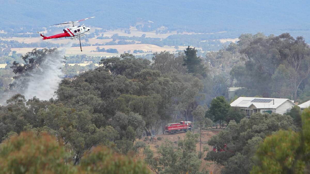 A helicopter drops water close to one of the homes under threat on Yarrabee Road. Picture: MARK JESSER