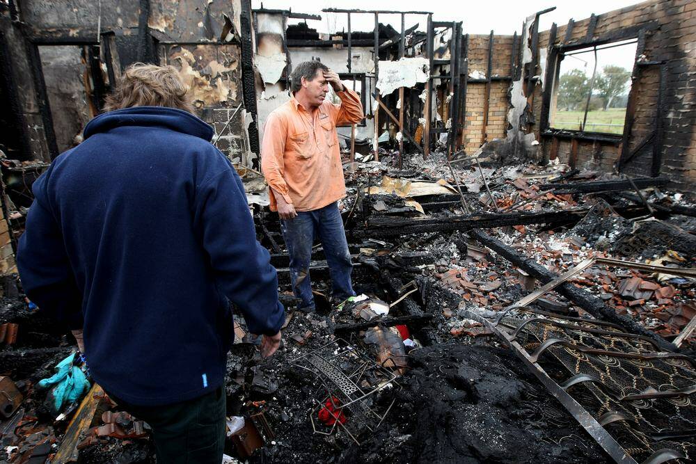 Glenn (orange shirt) and Brent Nicoll (blue) picks through the ruins of their father's Whorouly home after it was gutted by fire. Picture: JOHN RUSSELL