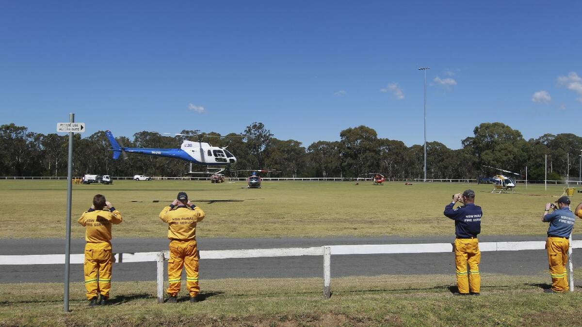 Firefighters at Bargo Oval in the Southern Highlands film a helicopter as it takes off on another water bombing mission. Picture: Sahlan Hayes, SMH News. 