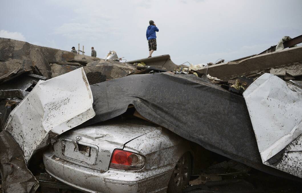 A damaged car is seen as a resident stands on top of wreckage after a tornado struck Moore, Oklahoma, May 20, 2013. Photo: REUTERS/Gene Blevins