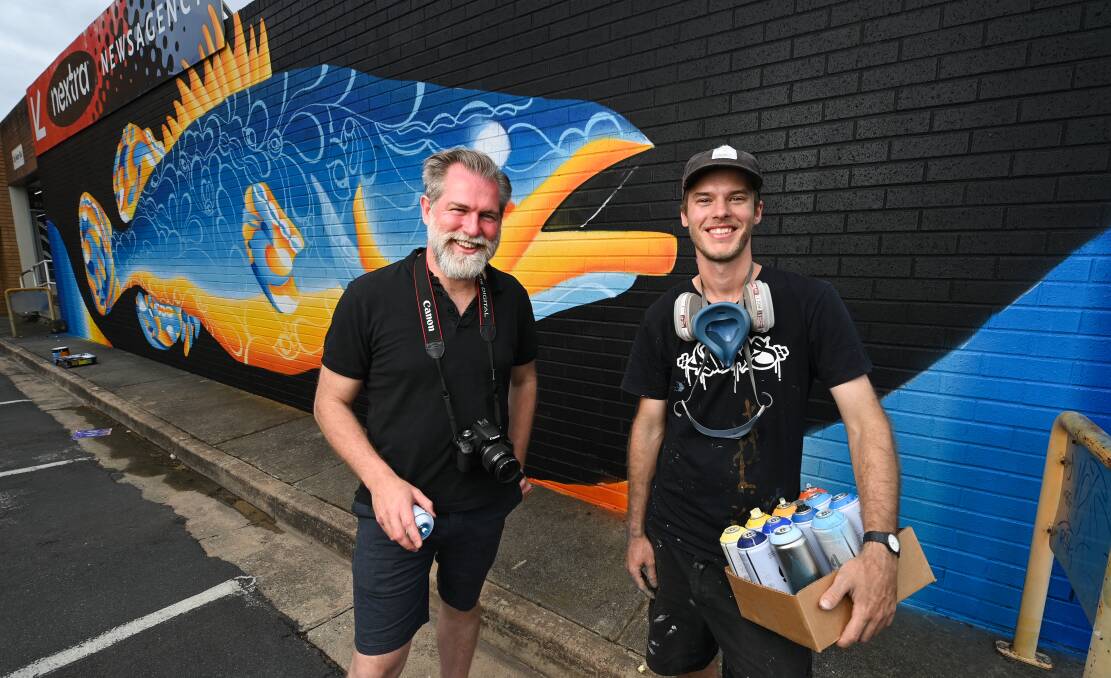FRESH FISH: Wodonga's Kieran Mahonywith artist Lukas Kasper in front of his Murray Cod mural on the wall of Mahony's Newsagency on High Street. Picture: MARK JESSER