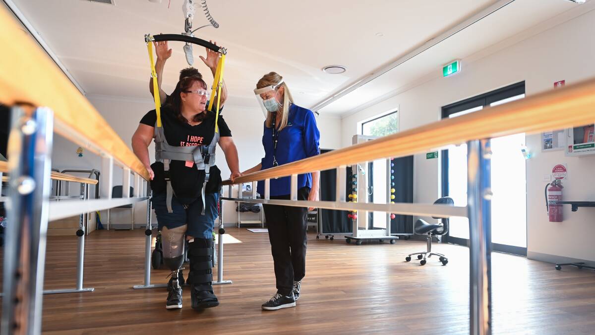 TAKING STRIDES: Disability advocate Kylie Paull upright at Icaria Health with the support of a hoist and physiotherapist Liesa Tighe. This is one of the few times a week Mrs Paull is able to fully stretch out her body and be free from her wheelchair. Picture: MARK JESSER