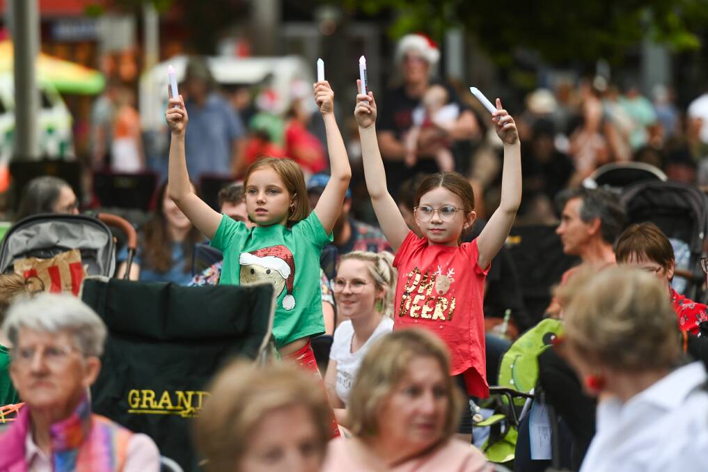 Isabelle Peacock, 9, and Maggie Skeers, 8, of Wodonga, get into the Christmas spirit at Carols by Candlelight at Albury's QEII Square on Wednesday, December 20. Picture by Mark Jesser