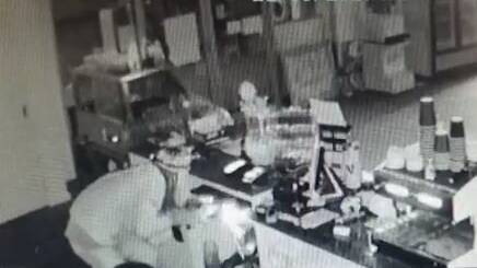 HANDYMAN THIEF: Sparks erupt from the cash drawer as the bandit uses his angle grinder to cut away the till from its fixtures below the store's counter.