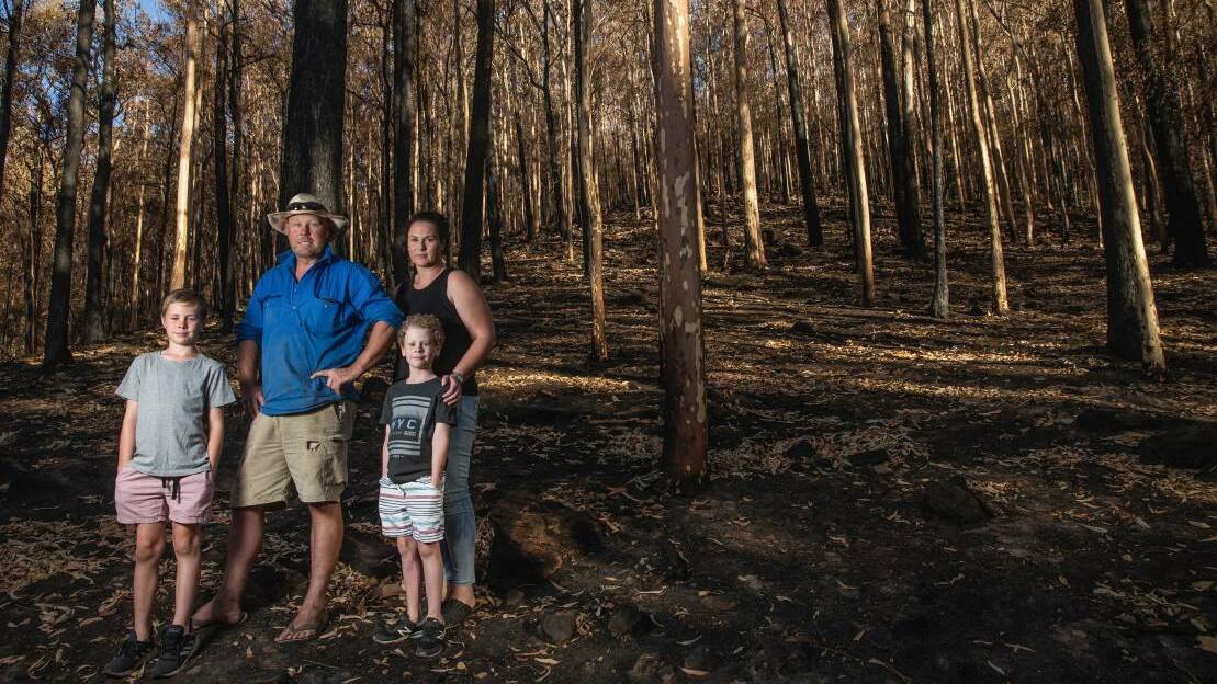 Joel and Leah Eddy, with their sons, Hudson and Tom, inspect the burnt bushland behind their Martinsville house. Picture: Marina Neil