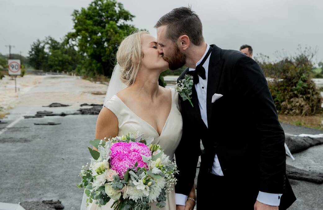 MIRACLE: Kate and Wayne Bell share a kiss in front of the flooded road which trapped them on the morning of their wedding. Photo: AMANDA HIBBARD