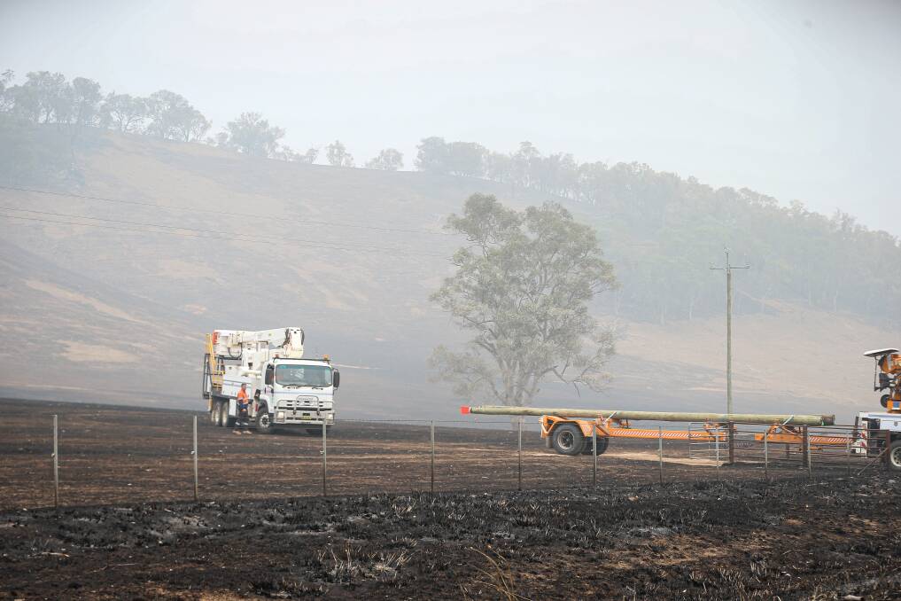 On the job: Essential Energy workers near Jingellic earlier in the week working on the replacement of power poles that were destroyed by flames travelling across farmland. Picture: JAMES WILTSHIRE