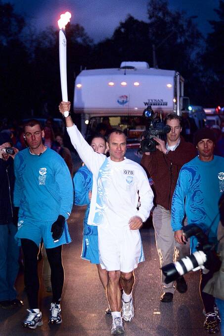 HERE IT IS: Paddler Tony Zerbst holds the torch aloft as he becomes the first torch bearer to complete a leg in NSW in 2000. Camera operators and photographers surrounded him as he went along the Union Bridge.