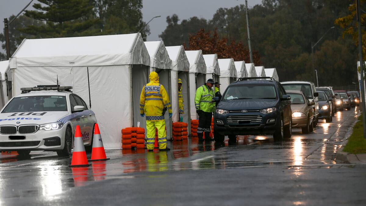 Gloomy shift: Police stop a line of cars entering NSW at Albury's Wodonga Place amid rainy conditions on Sunday morning. Picture: TARA TREWHELLA