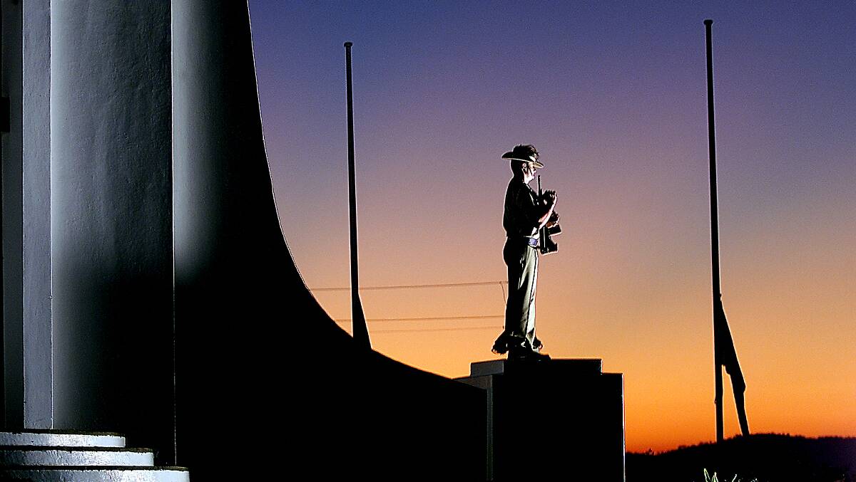 Solemnity personfied: A soldier stands in front of flags at half mast at Albury's war memorial on Anzac Day.