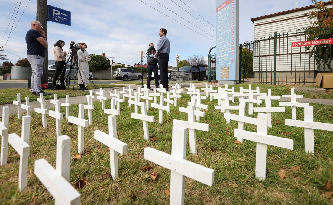Crosses, representing 68 lives lost while people were awaiting surgery at Albury Wodonga Health, sit in the ground as Bill Tilley speaks to the media at Wodonga hospital. Picture by James Wiltshire