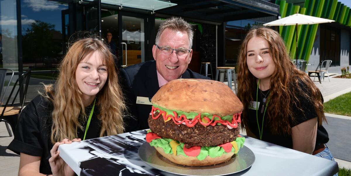 Cafe with the lot: Albury mayor Kevin Mack with youth representatives Milla Reid, 18, and Isabella Percy, 16, and the hamburger cake made by Jodie Saunders to mark the opening of the city's new youth eatery. Picture: MARK JESSER