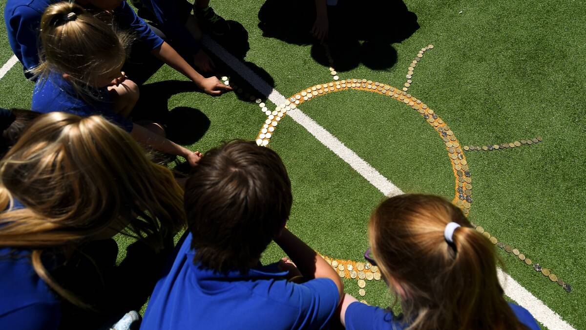 Hot topic: Students watch as their coins glisten after laying them out to form a sun at Thurgoona Public School on Monday afternoon. Picture: MARK JESSER