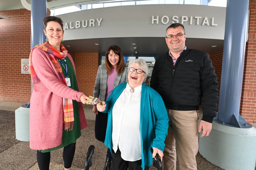 Sylvia Britt hands over her $100 winnings to Albury Wodonga Health Foundation manager Gina Bladon as 2AY radio hosts Kylie King and Kev Poulton watch on at the Albury hospital on Tuesday. Picture by Mark Jesser.