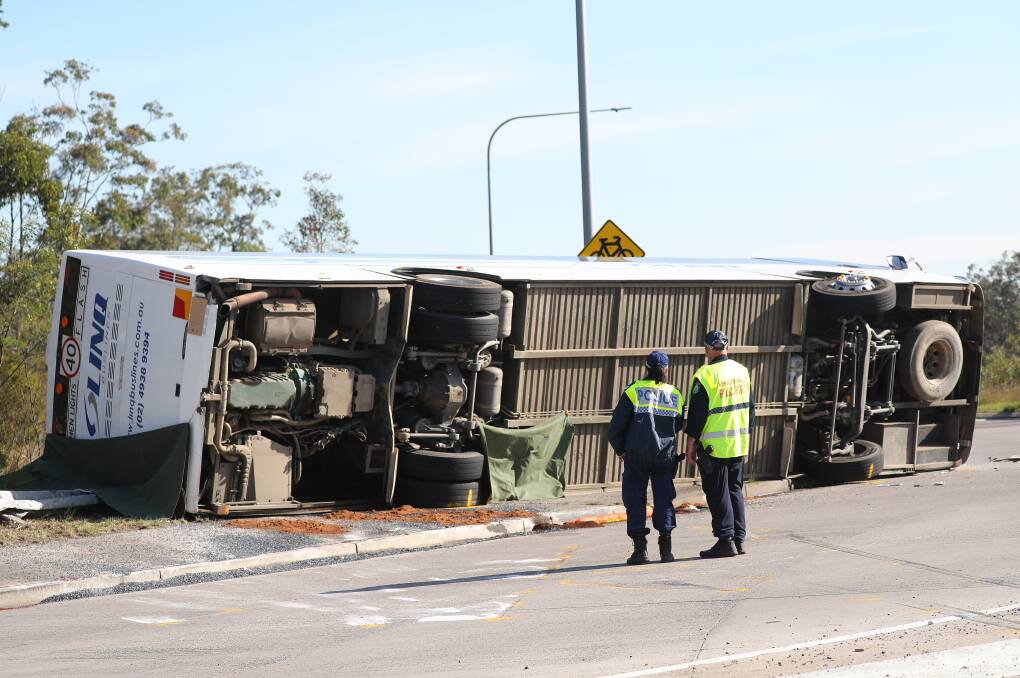 Police look over the flipped bus which overturned in the Hunter Valley. Its driver Brett Andrew Button has been charged over the crash and bailed. Picture from the Newcastle Herald