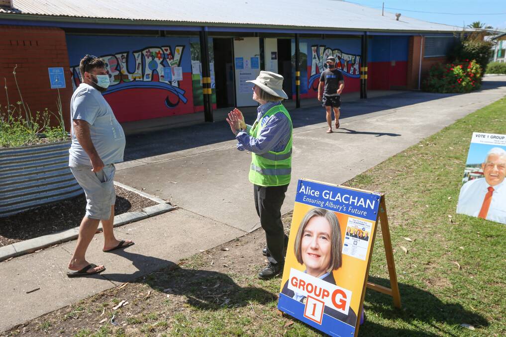 Sign of the times: Reflecting COVID's impact, a voter wears a mask while listening to councillor Alice Glachan at Albury North Public School. Picture: JAMES WILTSHIRE