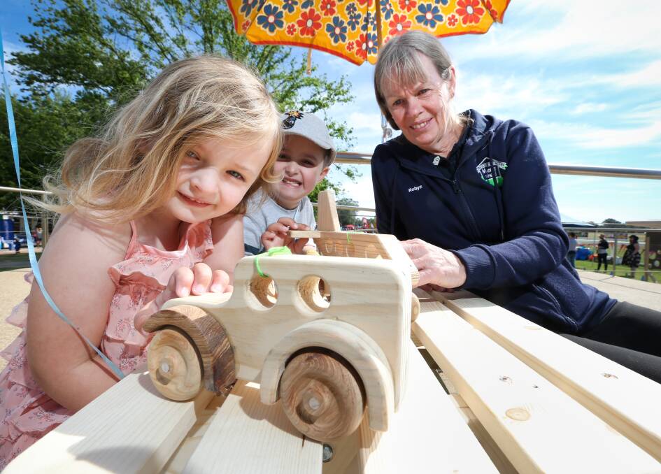 Joinery jalopy: Thurgoona's Caitlin Rodd, 4, and her brother Austin, 6, with a wooden car and Robyn Seabright who represents the Chiltern Men's Shed members who make such toys. Picture: KYLIE ESLER 