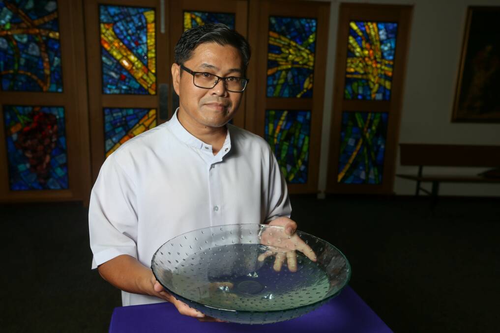 Removed: Father Junjun Anaya with the communal holy water used at Sacred Heart Catholic Church in Wodonga. It is now no longer be used as part of coronavirus prevention. Picture: TARA TREWHELLA