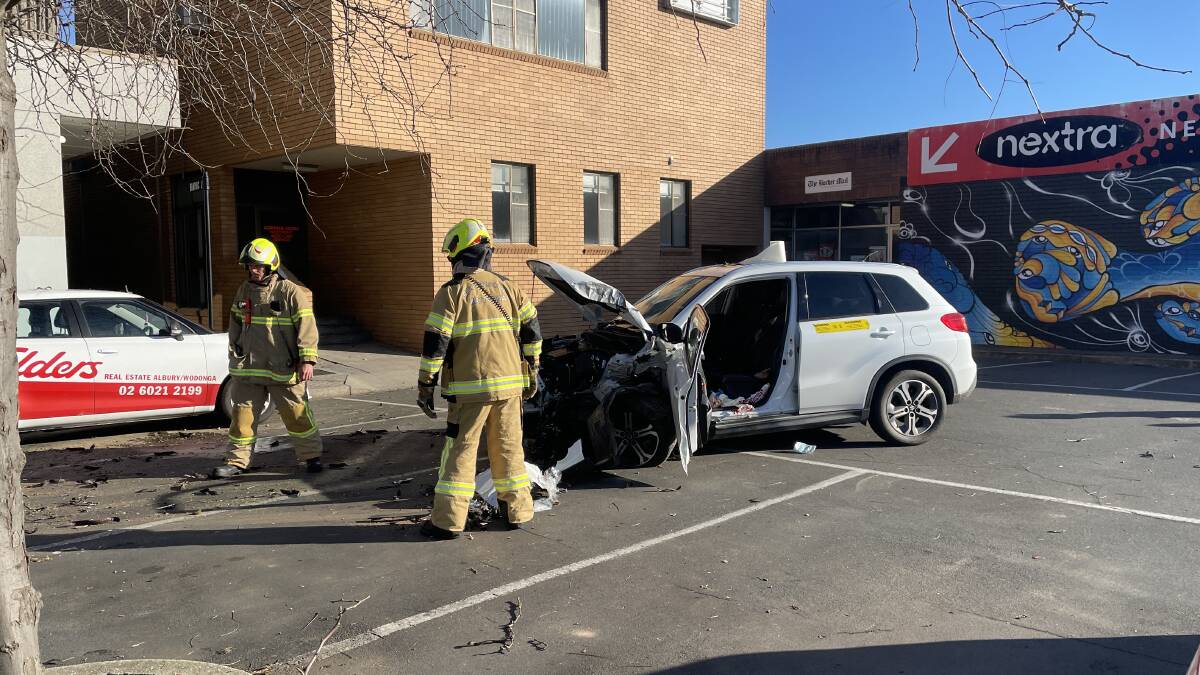 Cleaning up: Firefighters tidy away debris spread after this car struck a tree in the Wodonga car park at the rear of High Street shops including Mahony's Newsagency in the background.