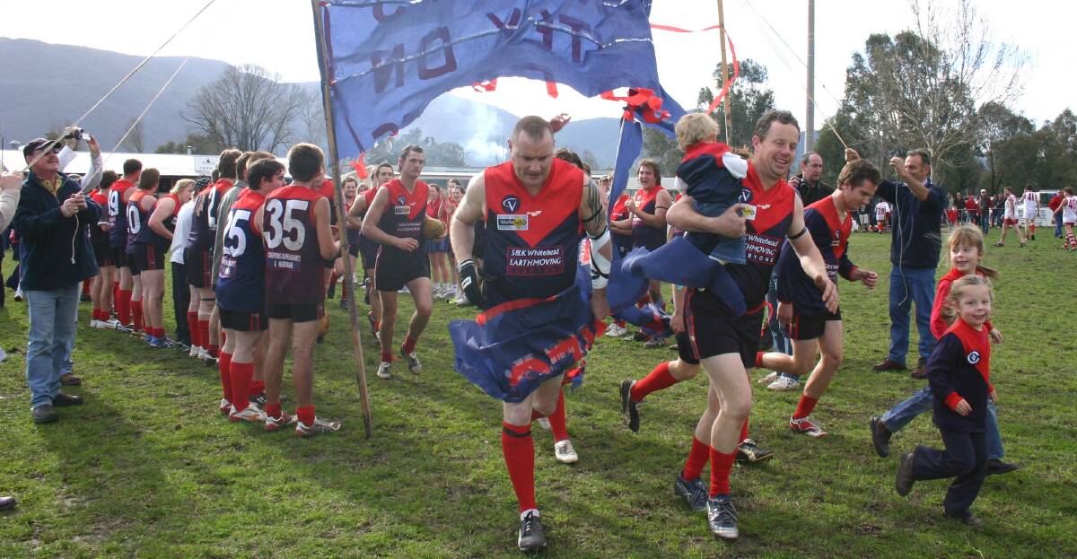 Former Corryong coach John Waldron and Andrew Whitehead run through the banner before Whitehead's 300th match.
