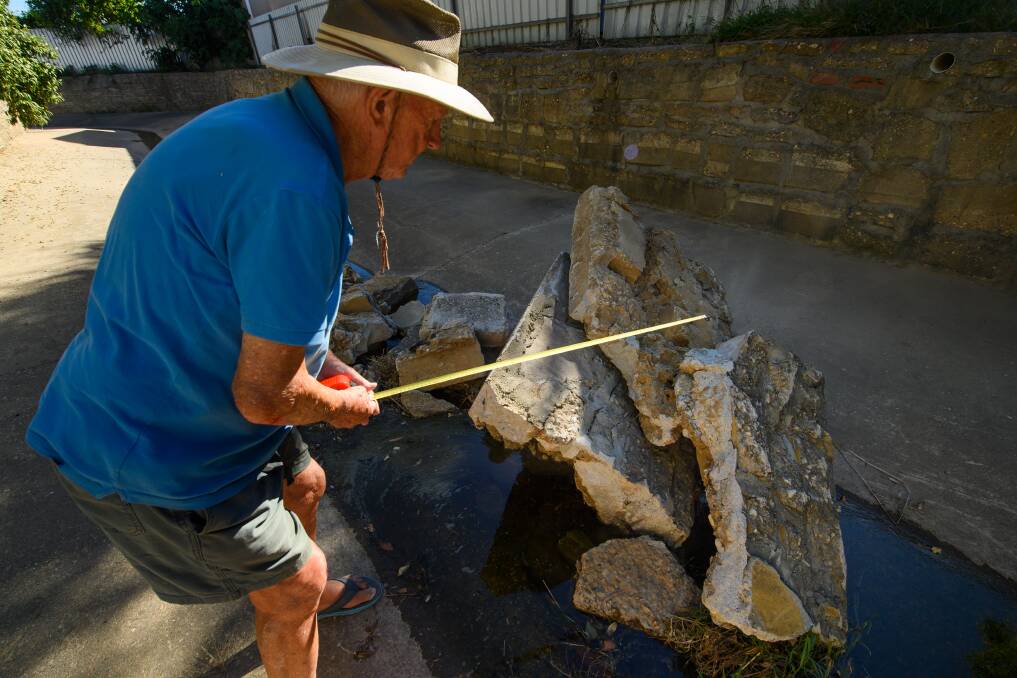 WASHED AWAY: Ray Dallinger measuring pieces of the broken concrete wall behind his North Albury home.
