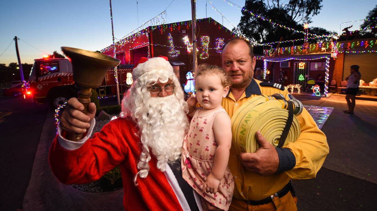 FIRING UP FOR CHRISTMAS: Santa drops in to help young Dakidoa Batty, 2, and Lavington Rural Fire Brigade captain Bruce Barnes celebrate the festive season at the brigade's annual display on Thursday night. Picture: MARK JESSER