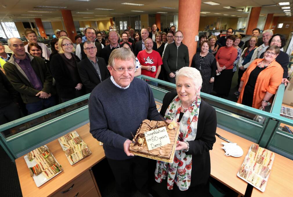 Darryl Starr and his partner Julie Pilkington hold a cake marking his 50 years at The Border Mail while surrounded by colleagues who downed tools for his morning tea yesterday. Picture: JOHN RUSSELL
