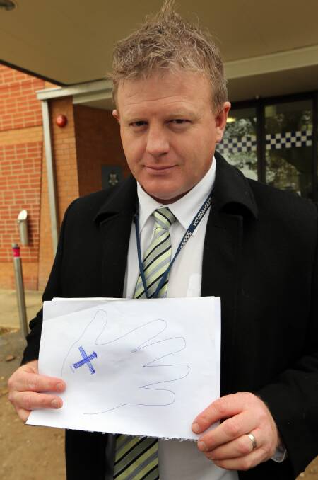 Acting Sgt Andrew Leonards shows a drawing of a tattoo on his hand of a cross that could link them to a person of interest. 