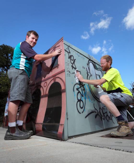 Signmaker Cameron Porter and signwriter Geoff Eberle apply anti-graffiti vinyl wrap to a utility box in Albury’s Gertrude Colquhoun Park yesterday. Picture: KYLIE ESLER