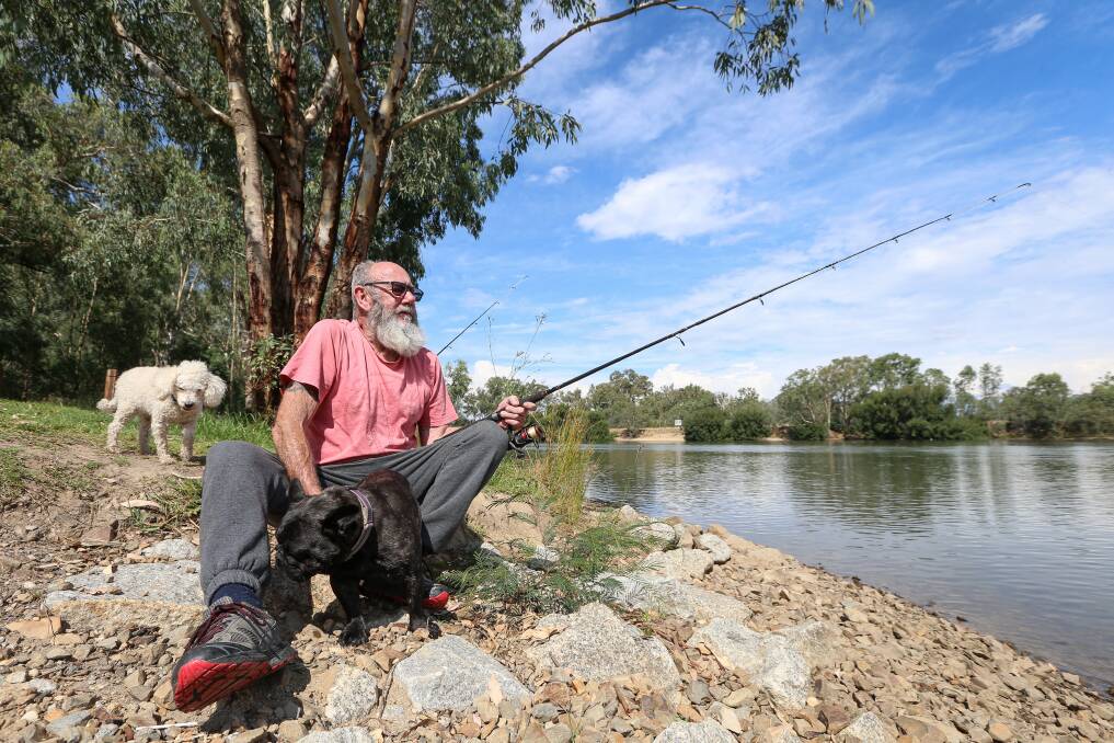 BLUE SKIES: Wodonga's Kevin Williams fishing with Olive and Fraggle at the Mungabareena reserve boat ramp. Picture: JAMES WILTSHIRE