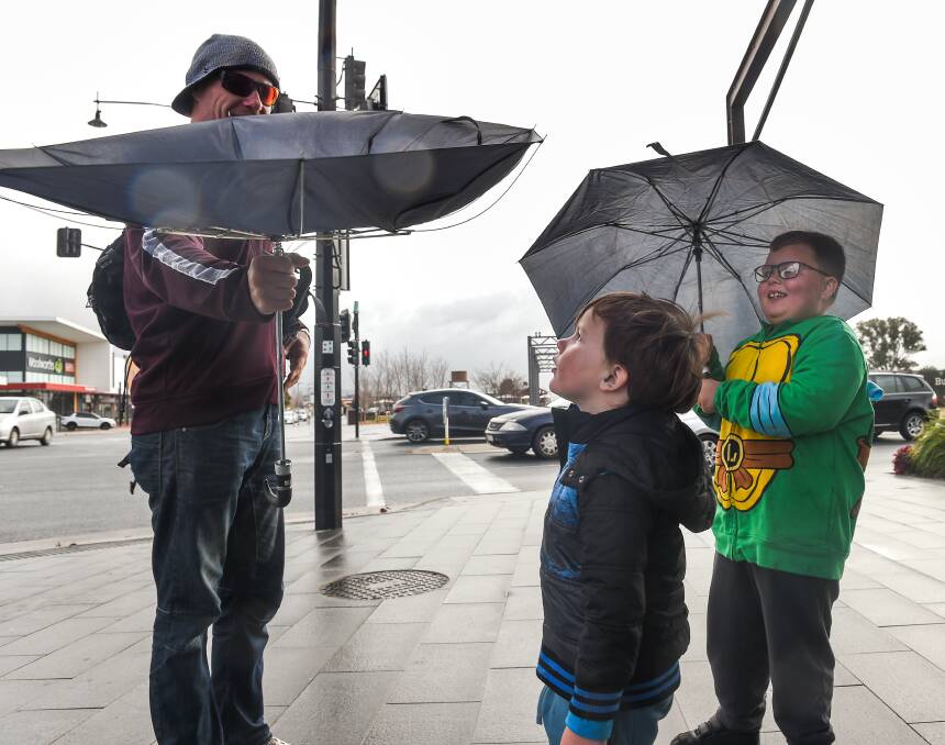 SHOCK: Wodonga's Tony Andrews shows sons Braxton, 4, and Hamish, 5, how the wind blew his umbrella inside-out. Strong winds are expected to continue across the weekend. Picture: MARK JESSER 