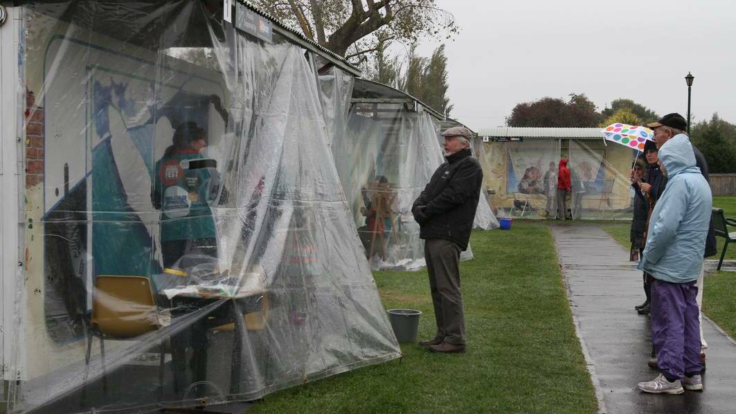 LAUNCESTON: Eamonn Matthews of Launceston chats with artists Patricia Smart and Ollie Grohs through the gap in their weather proof covering as a steady rain fell on day two of Mural Fest. Photo: Katrina Docking, The Advocate.