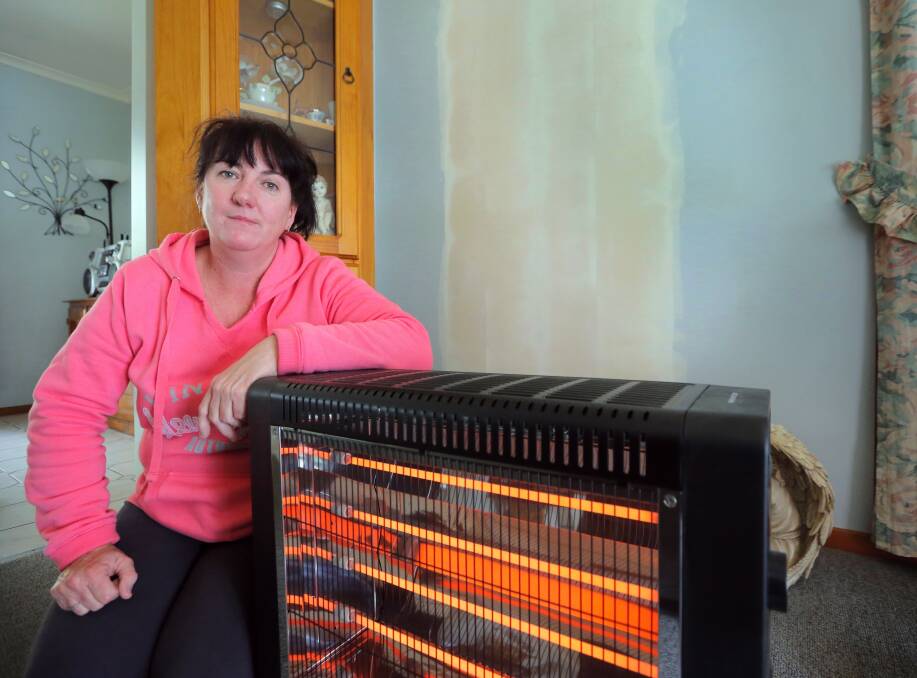 Caroline Merkel with an electric heater she has bought to provide some heat after her gas wall furnace was removed. The plaster on the wall behind her is where the wall furnace was. Picture: KYLIE ESLER