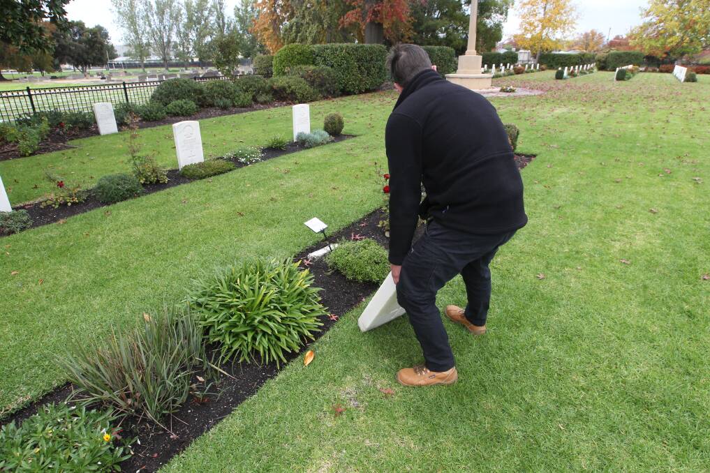 REPAIRS: A staff member from the Office of Australian War Graves lifts one of the damaged headstones at the cemetery. 