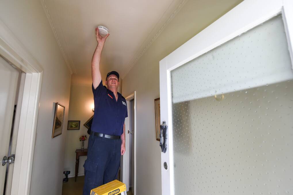 HELPING HAND: Firefighter Chris Davies replaces a smoke detector in an woman's home in Albury. There are plans to check 2000 houses this year. Picture: MARK JESSER
